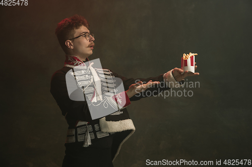 Image of Young man in suit as royal person isolated on dark green background. Retro style, comparison of eras concept. Beautiful male model like historical character, monarch, old-fashioned.