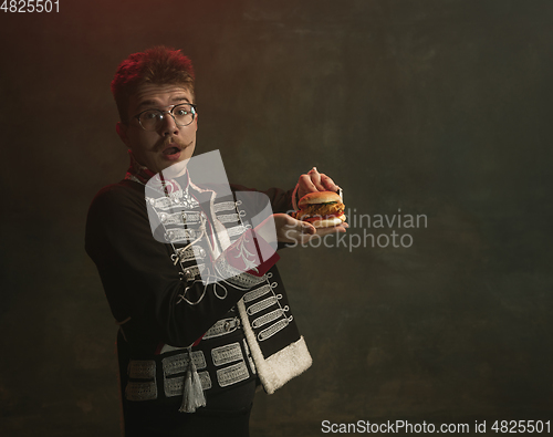 Image of Young man in suit as royal person isolated on dark green background. Retro style, comparison of eras concept. Beautiful male model like historical character, monarch, old-fashioned.