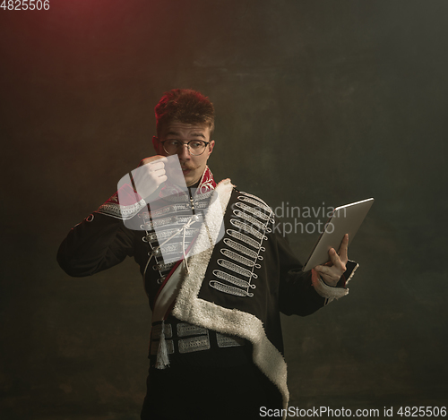 Image of Young man in suit as royal person isolated on dark green background. Retro style, comparison of eras concept. Beautiful male model like historical character, monarch, old-fashioned.