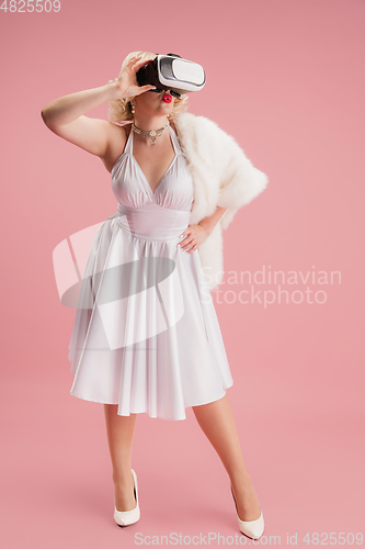 Image of Portrait of young woman in white dress on coral pink background. Female model as a legendary actress. Pin up. Concept of comparison of eras, modern, fashion, beauty.