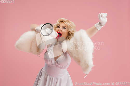 Image of Portrait of young woman in white dress on coral pink background. Female model as a legendary actress. Pin up. Concept of comparison of eras, modern, fashion, beauty.