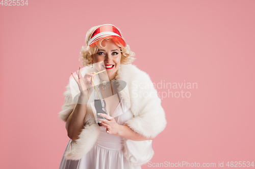 Image of Portrait of young woman in white dress on coral pink background. Female model as a legendary actress. Pin up. Concept of comparison of eras, modern, fashion, beauty.