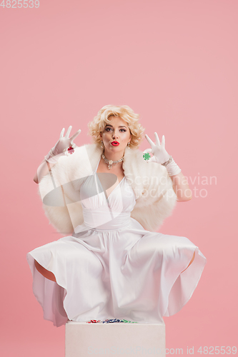 Image of Portrait of young woman in white dress on coral pink background. Female model as a legendary actress. Pin up. Concept of comparison of eras, modern, fashion, beauty.