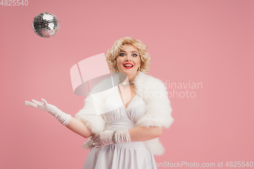 Image of Portrait of young woman in white dress on coral pink background. Female model as a legendary actress. Pin up. Concept of comparison of eras, modern, fashion, beauty.