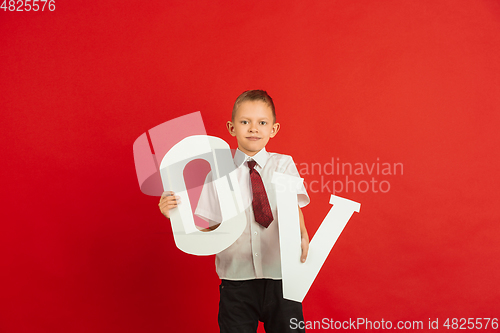 Image of Valentine\'s day celebration, happy caucasian boy holding letter on red background