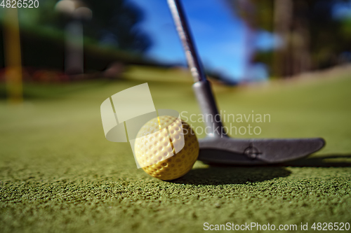 Image of Mini Golf yellow ball with a bat near the hole at sunset