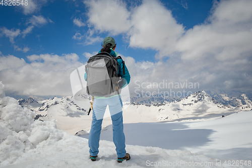 Image of Hiker woman standing up achieving the top. View at the snowy mou