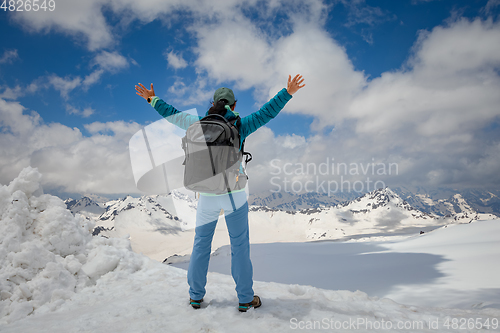 Image of Hiker woman standing up achieving the top. View at the snowy mou