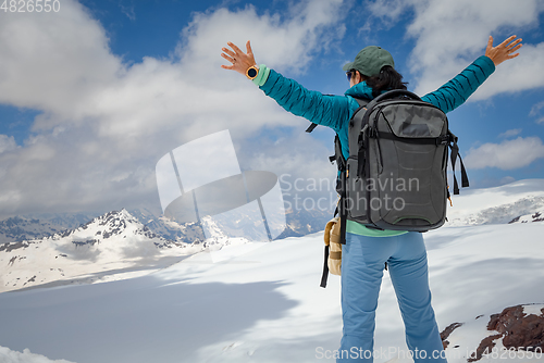 Image of Hiker woman standing up achieving the top. View at the snowy mou