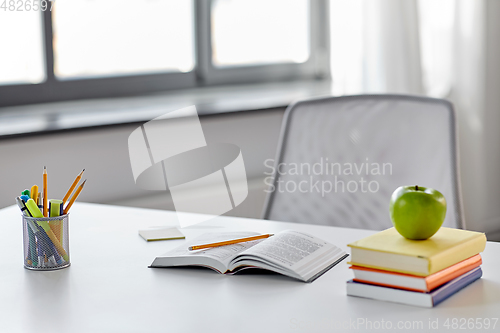 Image of books, apple and school supplies on table at home