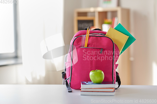 Image of pink backpack, apple and school supplies on table