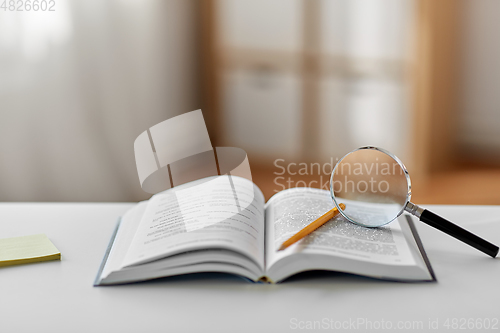 Image of book with magnifier and pencil on table at home