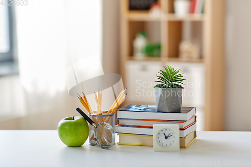 Image of books, magnifier, pencils, apple on table at home