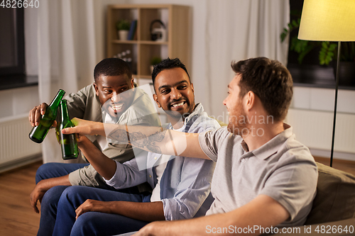 Image of happy male friends drinking beer at home at night