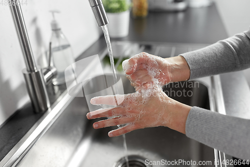 Image of woman washing hands with liquid soap in kitchen