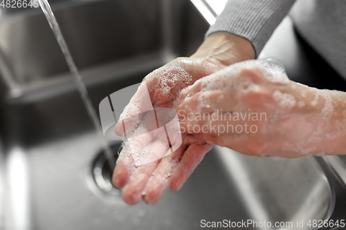 Image of woman washing hands with soap in kitchen