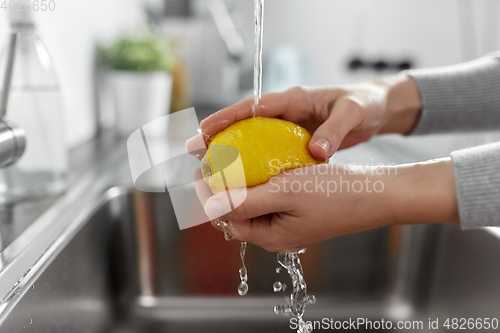 Image of close up of woman washing lemon fruit in kitchen