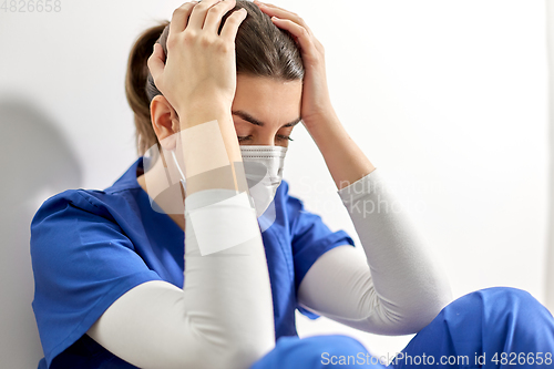 Image of sad doctor or nurse in face mask holding to head
