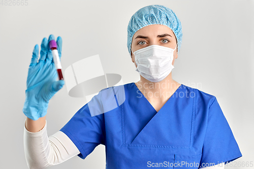 Image of doctor in face mask holding beaker with blood test