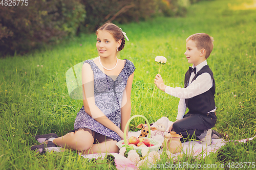 Image of Little boy and teen age girl having picnic outdoors
