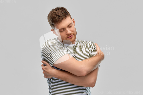 Image of happy young man in striped t-shirt hugging himself