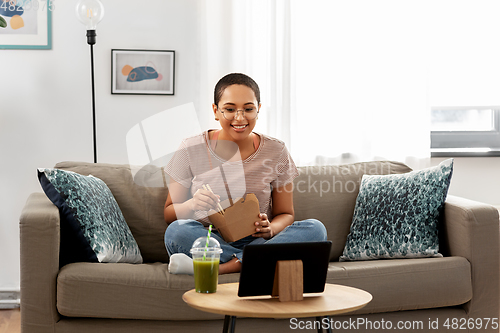 Image of african woman with tablet pc eating takeaway food