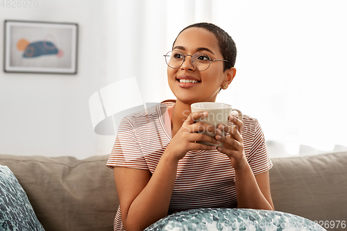 Image of happy african woman drinking tea or coffee at home