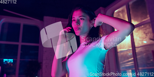 Image of Cinematic portrait of handsome young woman in neon lighted interior