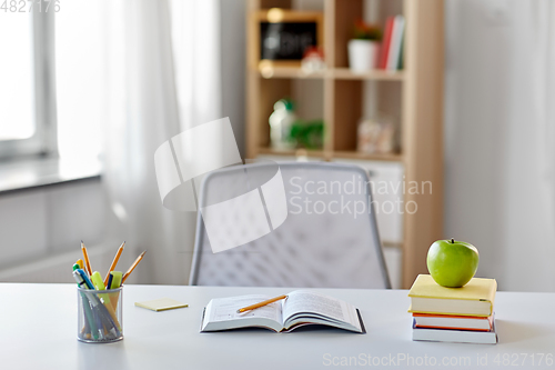 Image of books, apple and school supplies on table at home