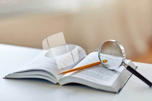 Image of book with magnifier and pencil on table at home