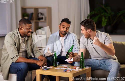 Image of male friends playing cards at home at night