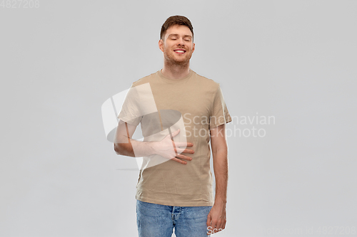 Image of happy full man touching tummy over gray background