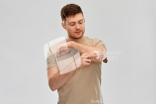Image of young man applying pain medication to his elbow
