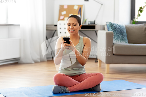 Image of woman with smartphone sits on exercise mat at home