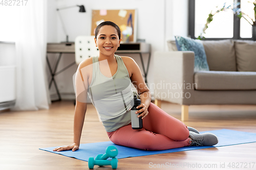 Image of smiling woman with bottle and dumbbells at home