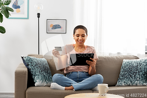 Image of happy woman with tablet pc and credit card at home