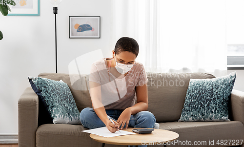 Image of woman in mask with papers and calculator at home