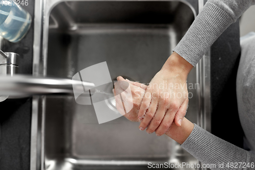 Image of woman washing hands with liquid soap in kitchen