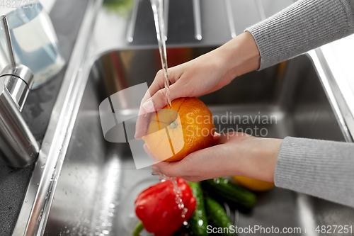 Image of woman washing fruits and vegetables in kitchen