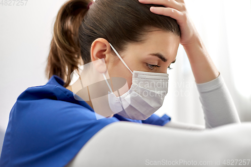 Image of sad doctor or nurse in face mask holding to head