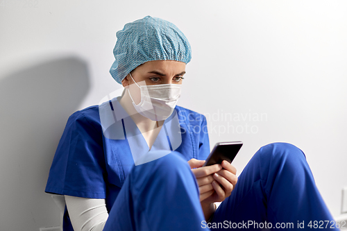 Image of sad doctor or nurse in face mask with smartphone