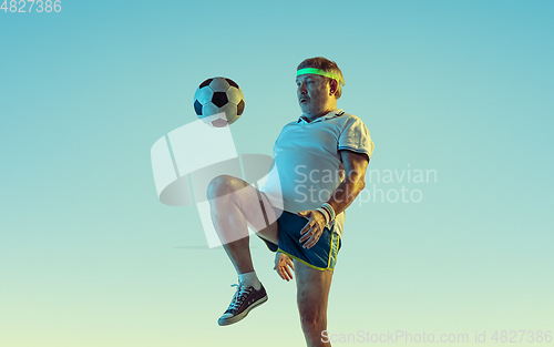 Image of Senior man playing football in sportwear on gradient background and neon light