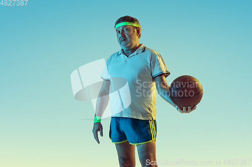 Image of Senior man playing basketball in sportwear on gradient background and neon light