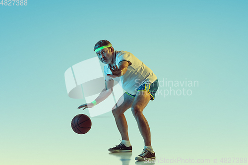 Image of Senior man playing basketball in sportwear on gradient background and neon light