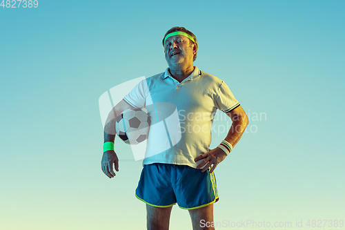 Image of Senior man playing football in sportwear on gradient background and neon light