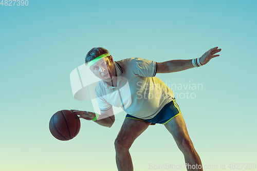 Image of Senior man playing basketball in sportwear on gradient background and neon light