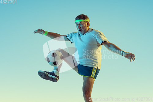 Image of Senior man playing football in sportwear on gradient background and neon light