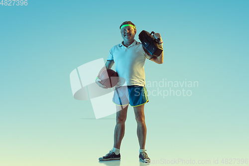 Image of Senior man posing stunning in sportwear with retro tape recorder on gradient background and neon light