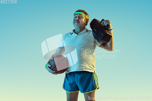 Image of Senior man posing stunning in sportwear with retro tape recorder on gradient background and neon light