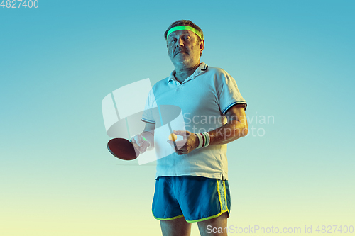 Image of Senior man playing table tennis in sportwear on gradient background and neon light